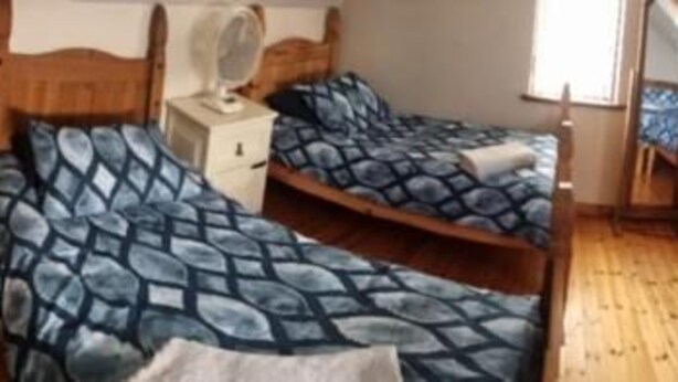 A room with two beds, a wooden floor, a chair, a desk, and a mirror. - Church View  (Ballycastle)
