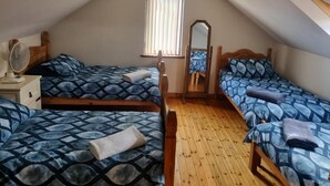 A dormitory room with two beds, a wooden floor, a window with blinds, a mirror, and a ceiling fan. - Church View  (Ballycastle)