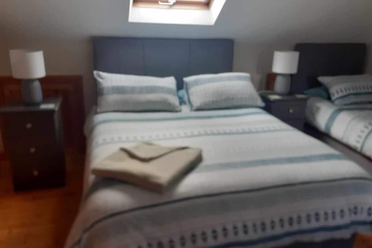 Un dormitorio con una cama, dos mesitas de noche, una lámpara en cada mesita y una ventana sobre la cama.