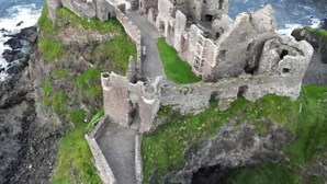 A historic stone castle ruin with a pathway leading to the entrance, surrounded by rocky terrain and overlooking a body of water. - Church View  (Ballycastle)