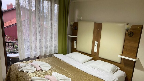 A hotel room with a bed, a window with sheer curtains, a small table, and a chair. - Sevimli suit konaklama (Amasra)