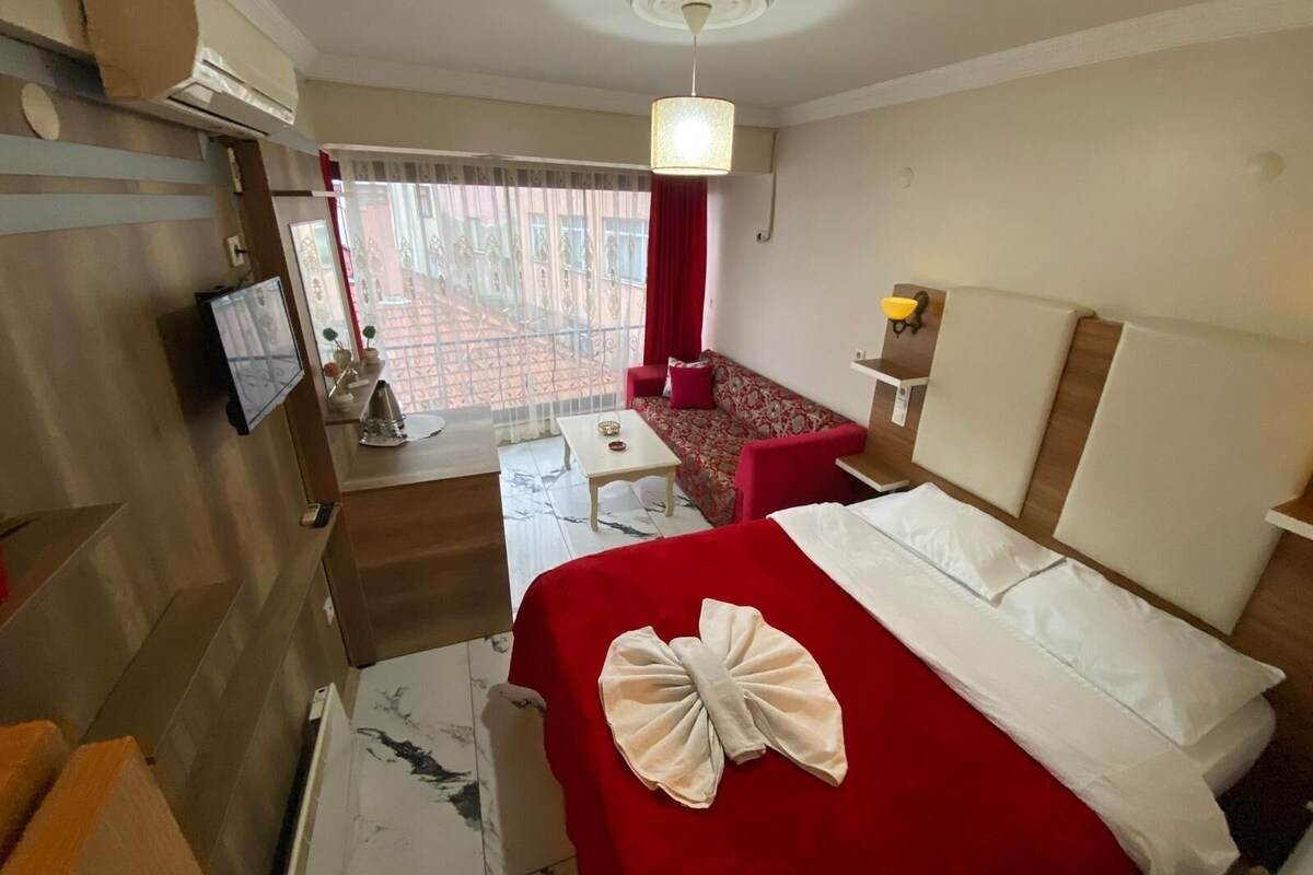 A hotel room with a bed, a desk, a chair, a TV, and a view of the outside.
