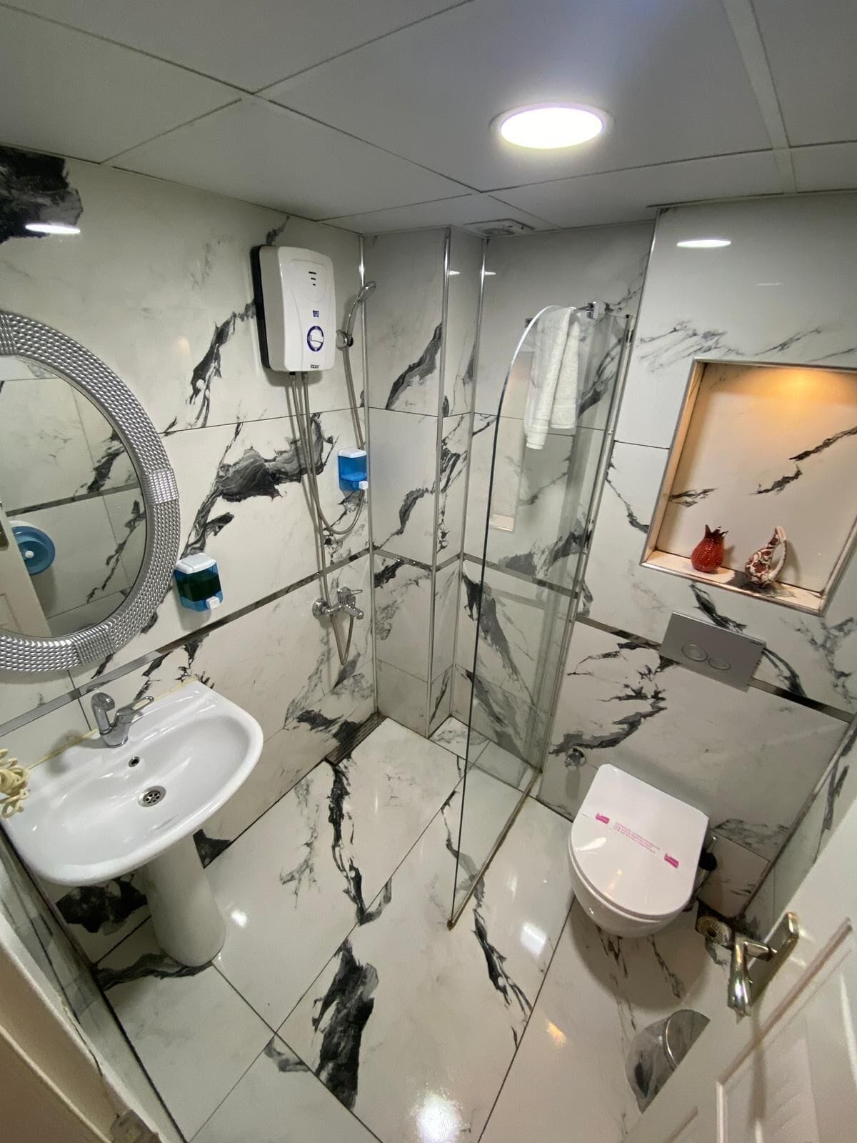 Une salle de bain avec un sol en marbre, un lavabo, des toilettes, un espace douche et un miroir.