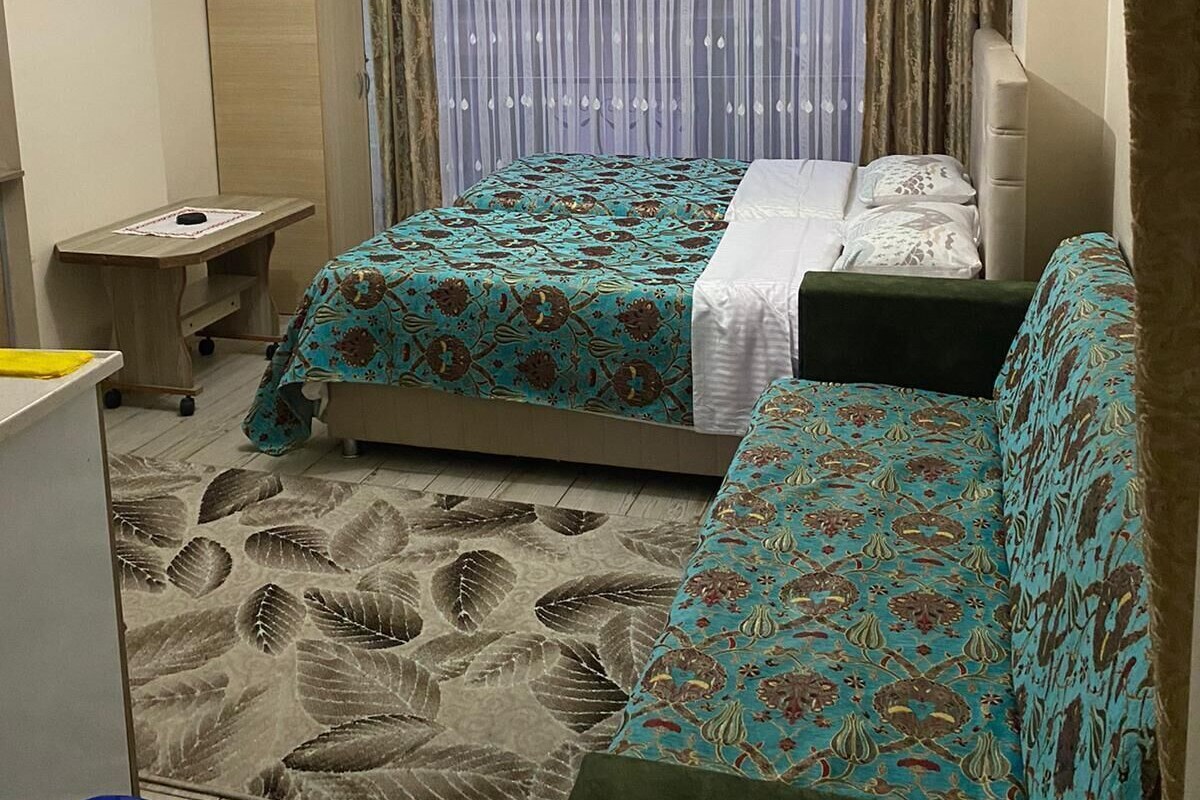 A hotel room with a bed, a sofa, a desk, a chair, a wardrobe, and a ceiling fan.