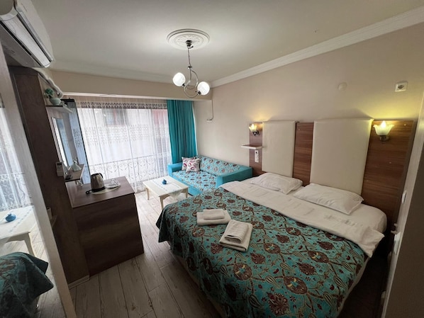 A hotel room with a bed, a desk, a chair, a mirror, a window with curtains, and a ceiling fan.