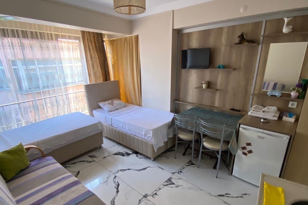 A hotel room with a bed, a desk, a chair, a TV, and a small refrigerator.