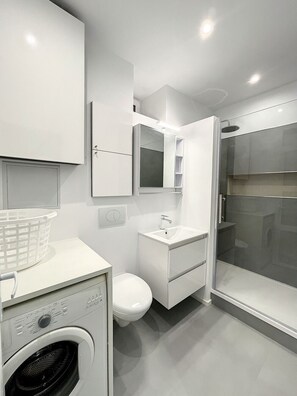 Ein modernes Badezimmer mit Waschmaschine, Toilette und Duschbereich.