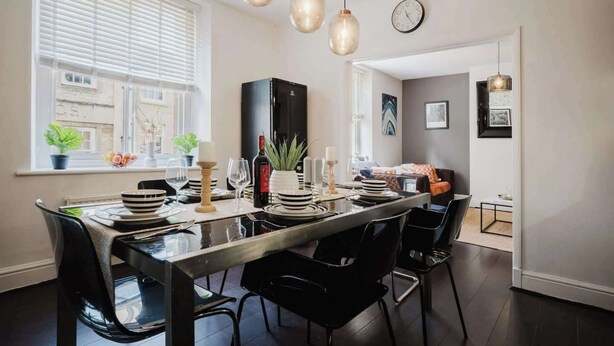 Un espace de salle à manger moderne avec une longue table, des chaises noires et des luminaires suspendus.