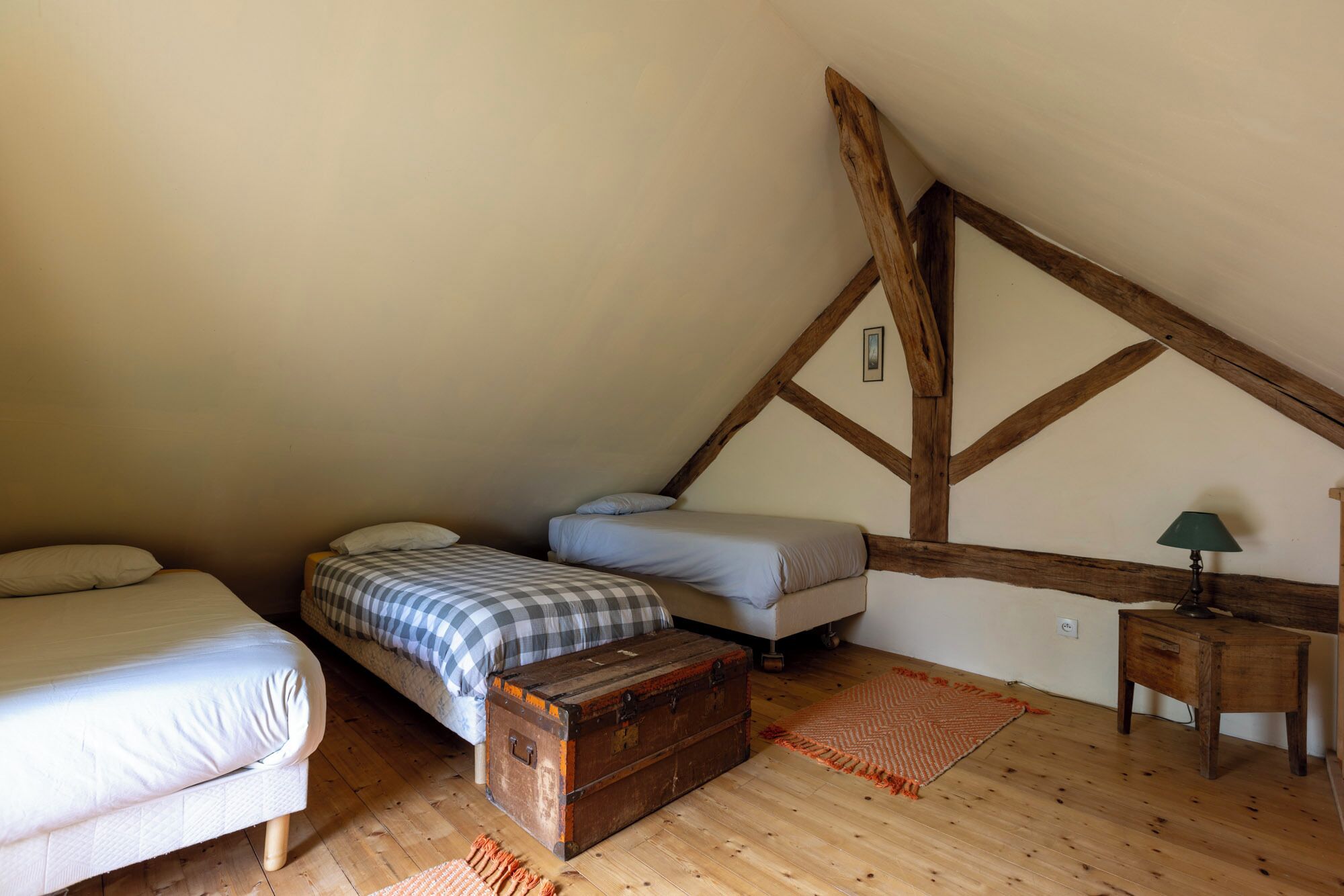 Een slaapkamer met twee bedden, een houten kist, een lamp en een klein tafeltje.