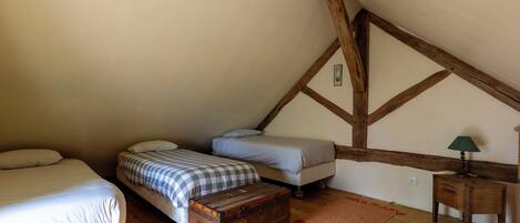 A bedroom with two beds, a wooden chest, a lamp, and a small table.