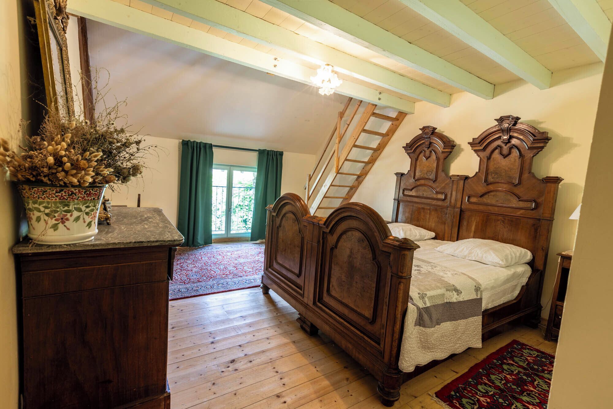 A bedroom with a wooden bed, a dresser, a potted plant, a window with curtains, and a wooden ceiling.