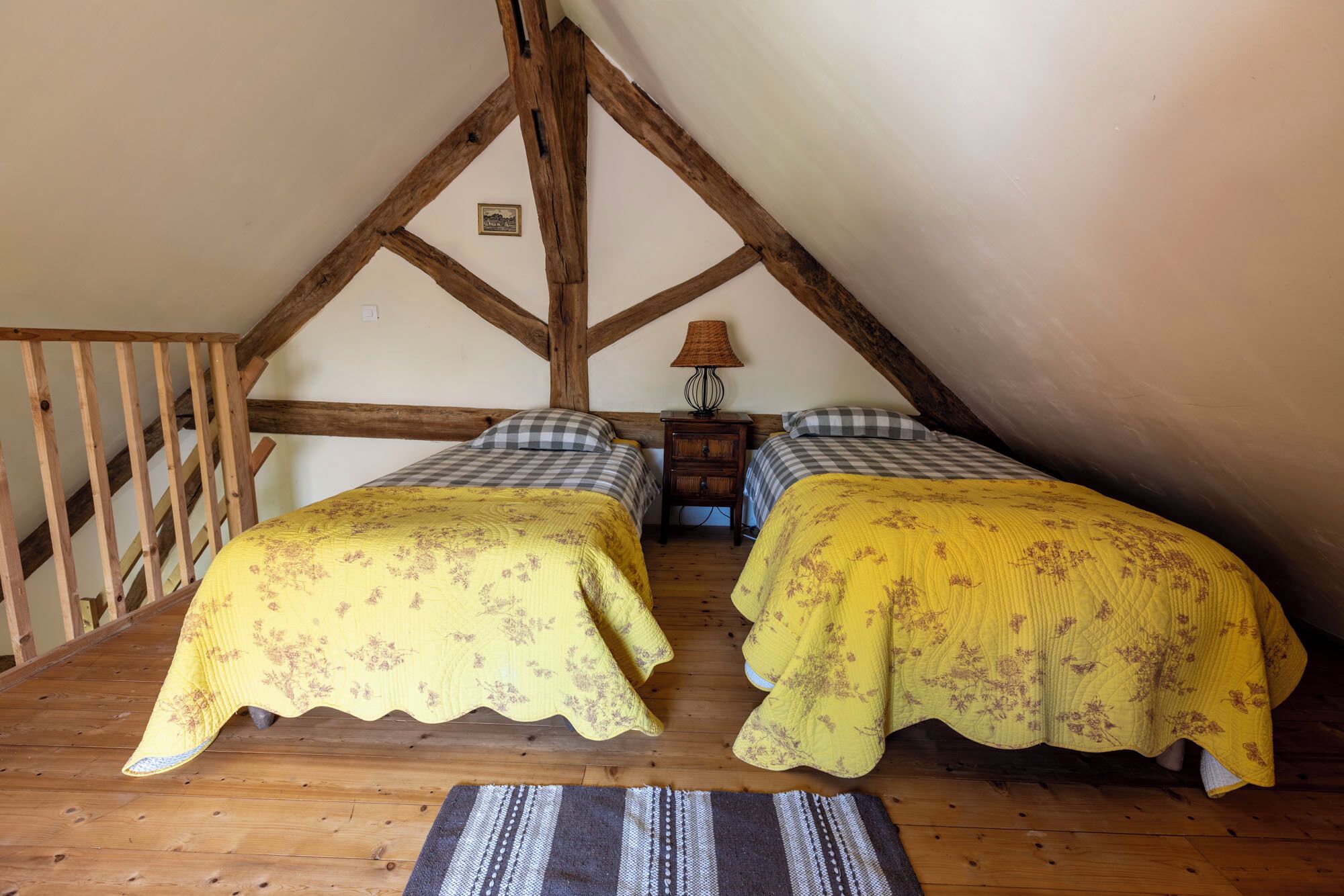 A room with two beds, wooden beams, a lamp, and a small table.