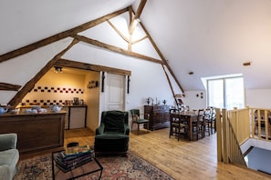 Une piĂšce de style loft avec des poutres apparentes, un coin cuisine, une table Ă manger avec des chaises et un escalier.