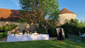 An outdoor event with a table set for a meal, surrounded by greenery and a historic building with a tower.