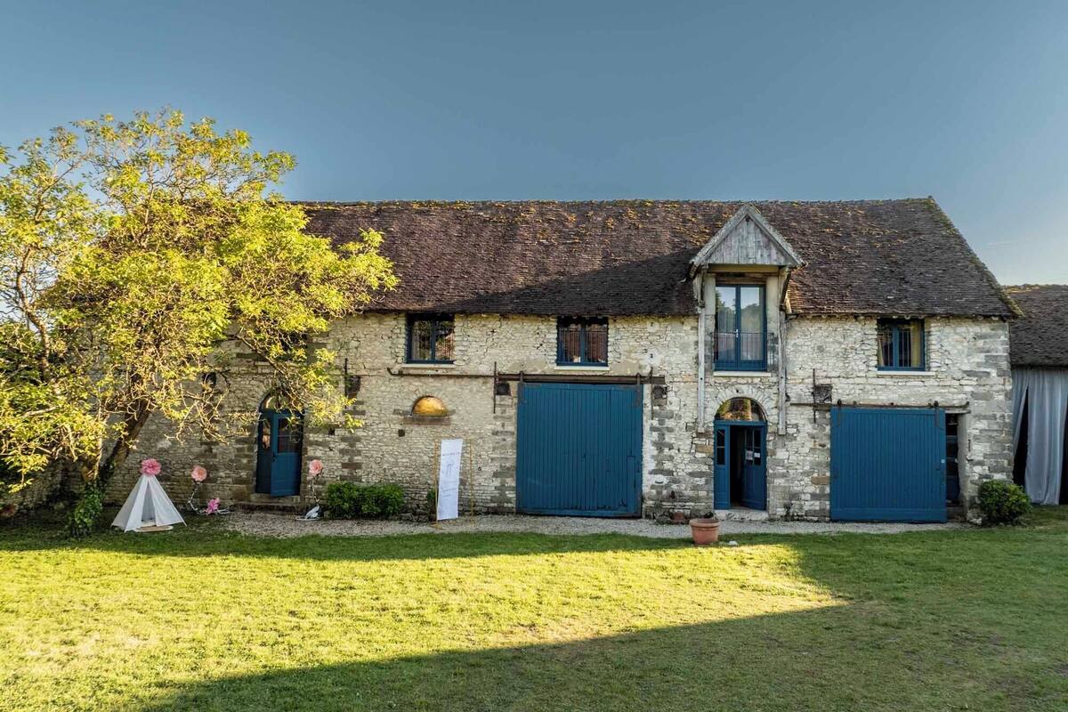 A stone farmhouse with a central chimney, two blue garage doors, and a small porch.