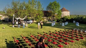 An outdoor event with chairs arranged in rows, a building with a tower, and trees in the background.