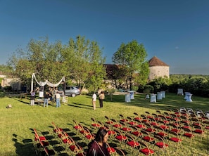 Un Ă©vĂ©nement en plein air avec des chaises disposĂ©es en rangĂ©es, un bĂątiment dotĂ© dâune tour et des arbres en arriĂšre-plan.