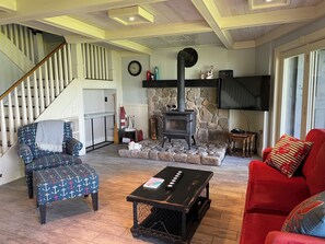 A living room with a staircase, a stone fireplace, a television, and a red sofa.