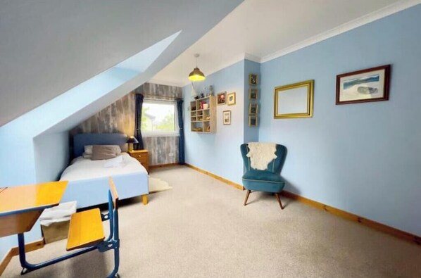 A bedroom with a bed, desk, chair, and a sloped ceiling.