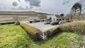 A parking area with cars, a building with a sloped roof, and a grassy landscape with hills in the background. - Spacious Family Retreat with Stunning Loch Views near Portree (Portree)