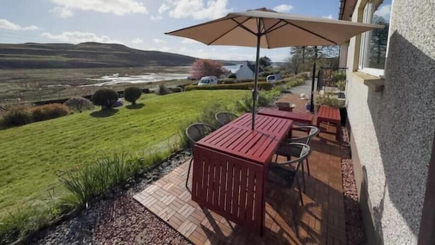 A patio with a table and chairs, a large umbrella, and a view of a lake and hills. - Spacious Family Retreat with Stunning Loch Views near Portree (Portree)