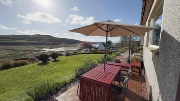 A patio with a table and chairs, a large umbrella, and a view of a lake and hills.