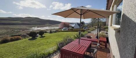 A patio with a table and chairs, a large umbrella, and a view of a lake and hills.
