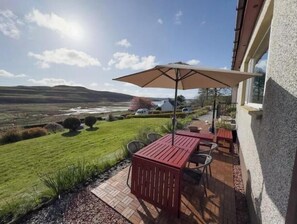 A patio with a table and chairs, a large umbrella, and a view of a lake and hills.