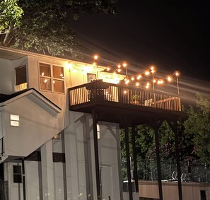 A two-story house with a balcony, string lights, and a fence. - Stunning lake property with a pool (Hot Springs)