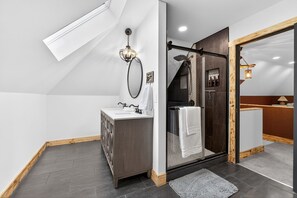 Un baño moderno con cabina de ducha de vidrio, tocador de madera y un espejo grande.