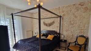 A bedroom with a four-poster bed, a stone wall, a chair, and a nightstand.