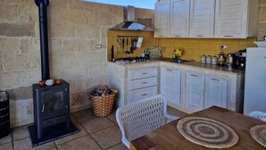 A rustic kitchen with a wood-burning stove, white cabinets, and a yellow-tiled backsplash.