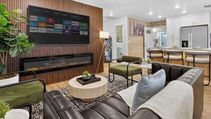 Ein modernes Wohnzimmer mit Flachbildfernseher, Kamin, Essbereich mit Barhocker und Küche mit weißen Schränken.