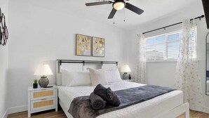 Ein Schlafzimmer mit einem Bett, zwei Nachttischen, einem Deckenventilator und Kunstwerken an der Wand.