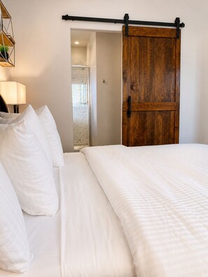 A bedroom with a large bed, a wooden door, and a hallway leading to a bathroom. - Rawhide Getaway - Detached Guesthouse (Prescott)