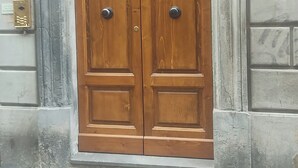 Eine doppelte Holztür mit einem Metallgriff, ein Fenster darüber und die Hausnummer 5 rechts.
