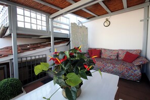 Une pièce avec une table blanche, un canapé à motifs, une plante en pot et une fenêtre donnant sur un beau paysage.