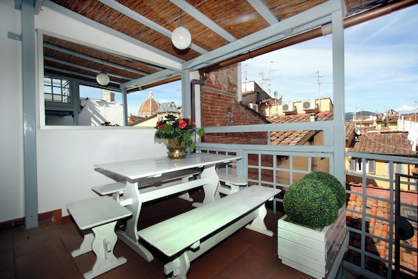 A balcony with a white table and benches, a potted plant, and a view of the cityscape. - Nest by the Medici Chapels - Attico (Firenze)