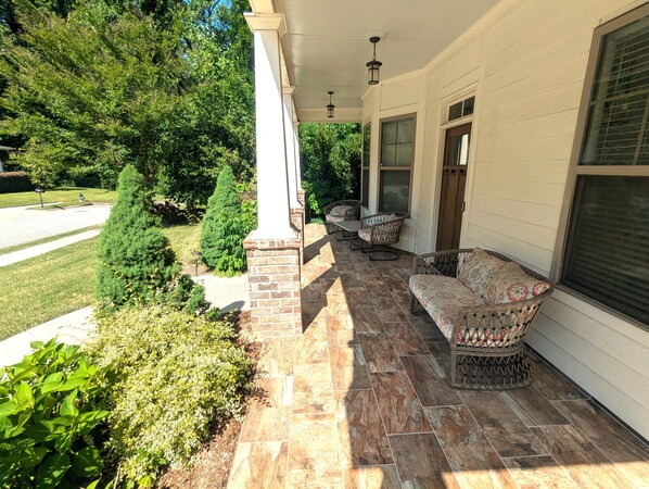 A covered porch with stone flooring, wicker furniture, and a view of a green landscape.