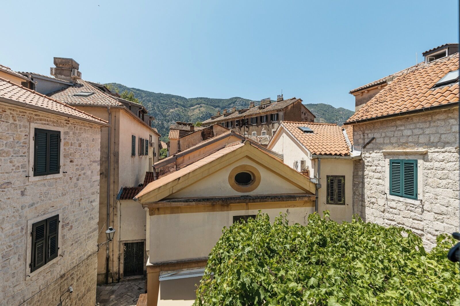 Una calle estrecha con edificios de piedra, una iglesia con campanario y una montaña al fondo.