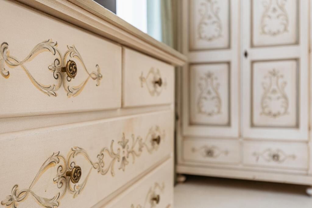 Une commode blanche aux poignées décoratives et un meuble avec des portes miroir et des panneaux décoratifs.