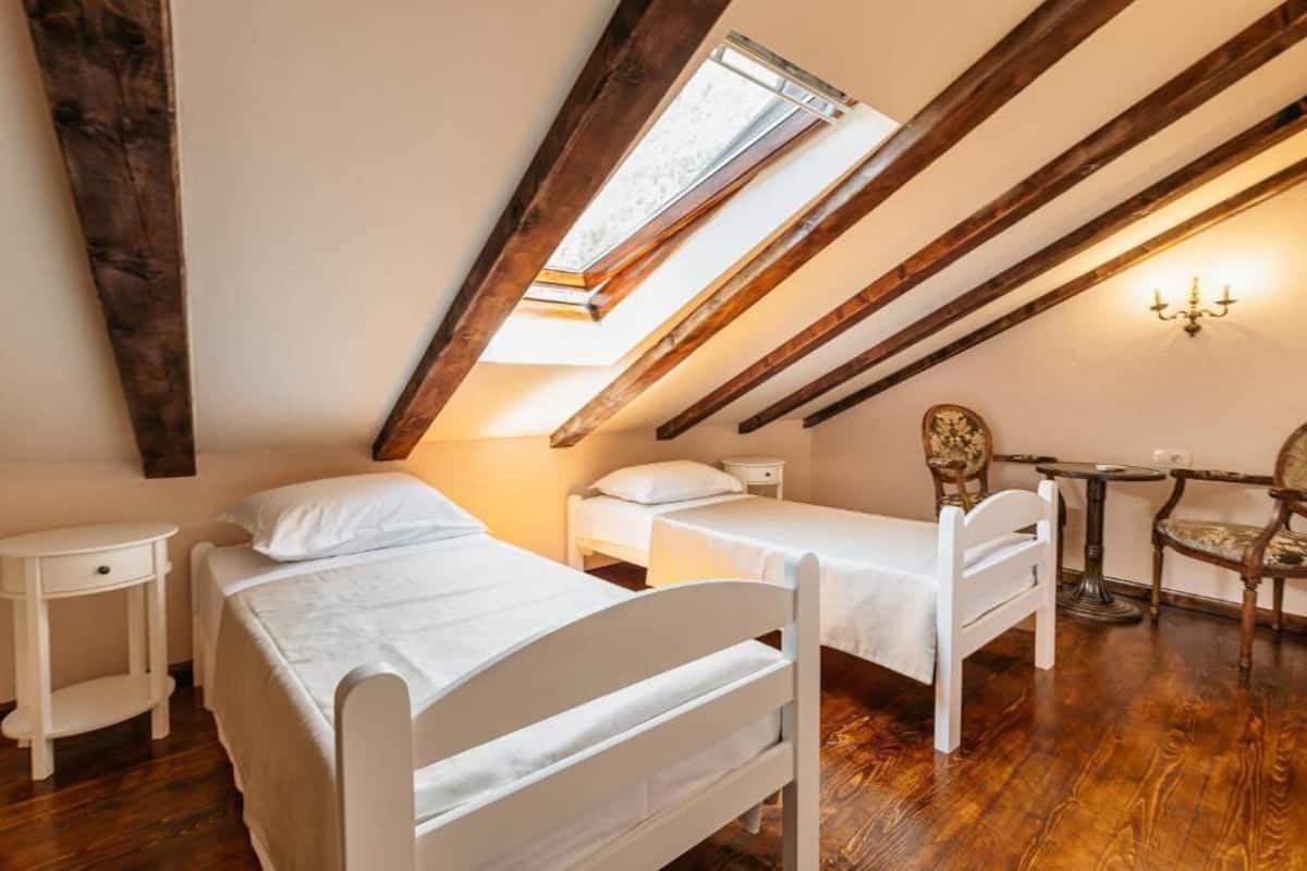 Una habitación con dos camas blancas, una mesita, una silla y una araña.