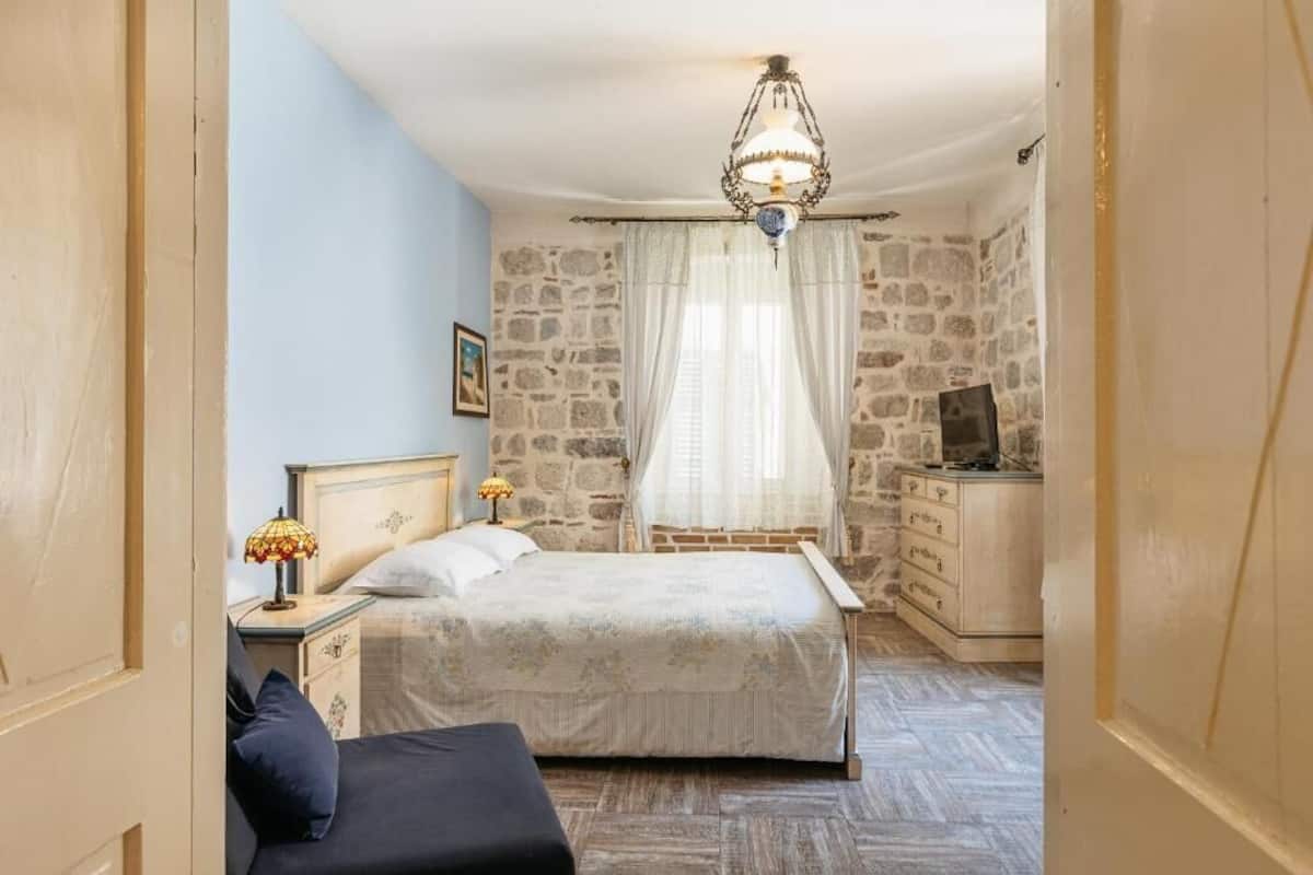 Un dormitorio con cama, mesita de noche, cómoda, televisor y pared de piedra.