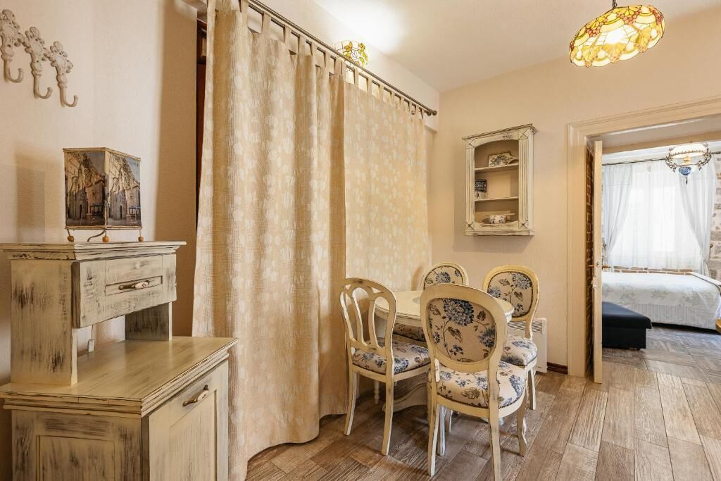 Um quarto com piso de madeira, uma mesa de jantar com cadeiras, uma cama com dossel, um espelho e um lustre.