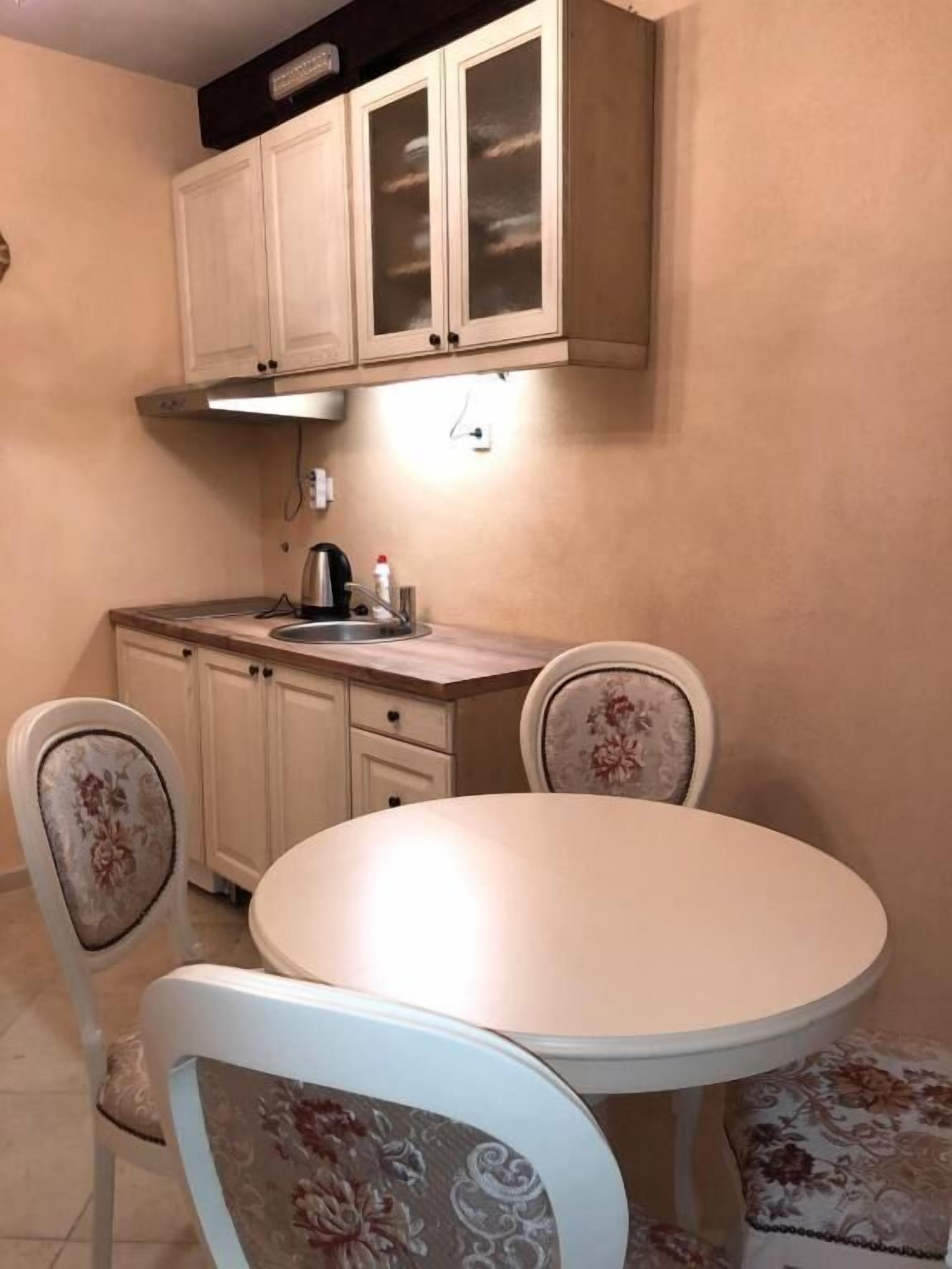 A small kitchen with a round table, two chairs, a stove, and cabinets.