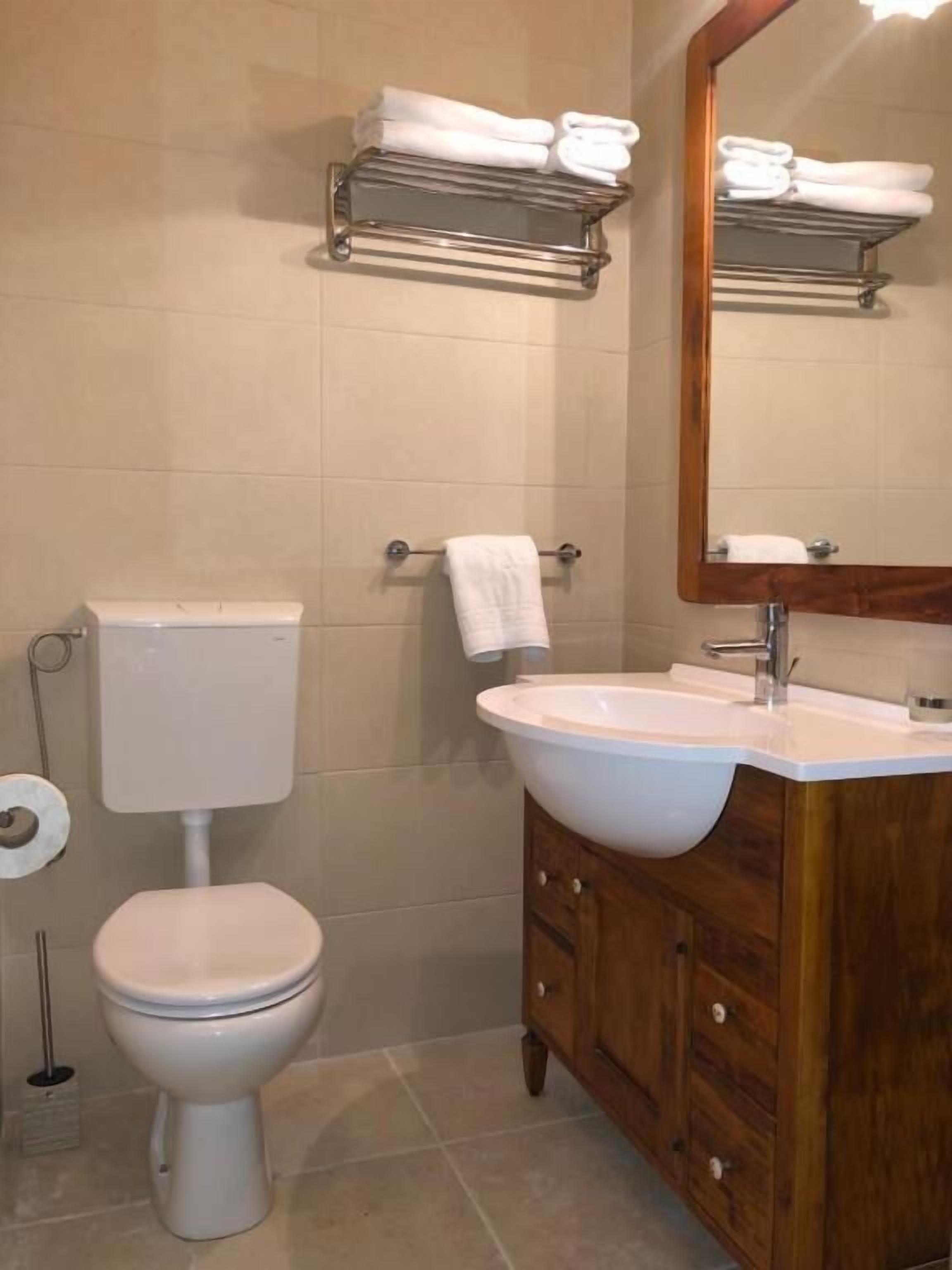 Un baño con inodoro, lavamanos, espejo y toallero.