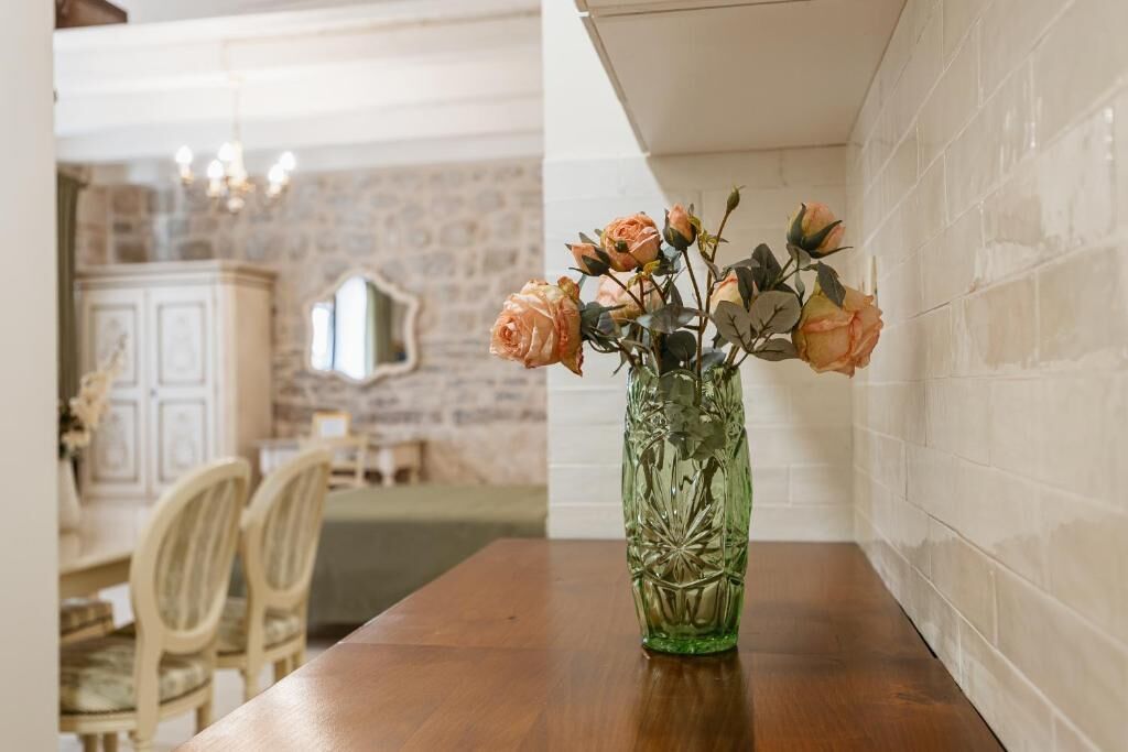 Una mesa de comedor con un florero verde que contiene rosas, un muro de piedra y una zona de comedor con sillas y una mesa.