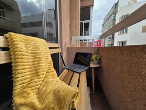 Ein kleiner Balkon mit einer Holzbank, einem gelben Handtuch, einem Laptop und einem Blumentopf.