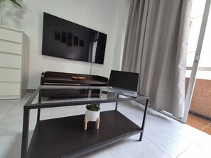 Ein modernes Wohnzimmer mit einem Glastisch, einem Laptop, einem Flachbildfernseher und einer Topfpflanze.