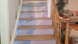 Un escalier avec des marches en bois et une rampe, menant à un palier où se trouvent un canapé et un vase de fleurs.